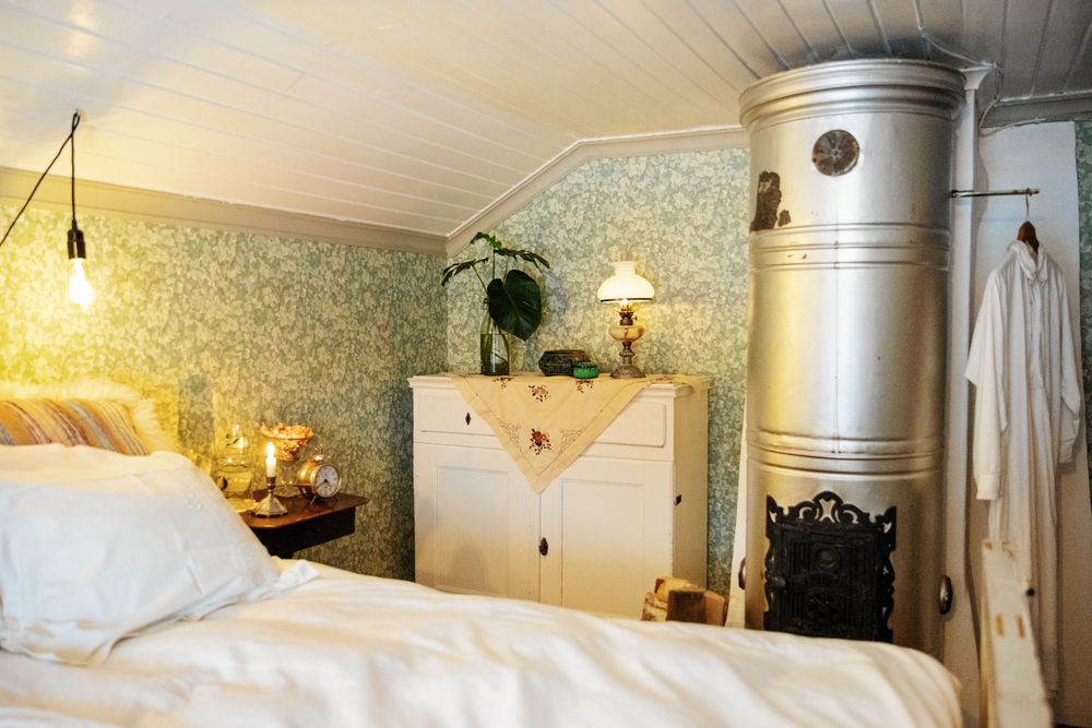 Mönstrade, gammeldags tapeter även i sovrummet med sin tidstypiska metallmålade kakelugn.