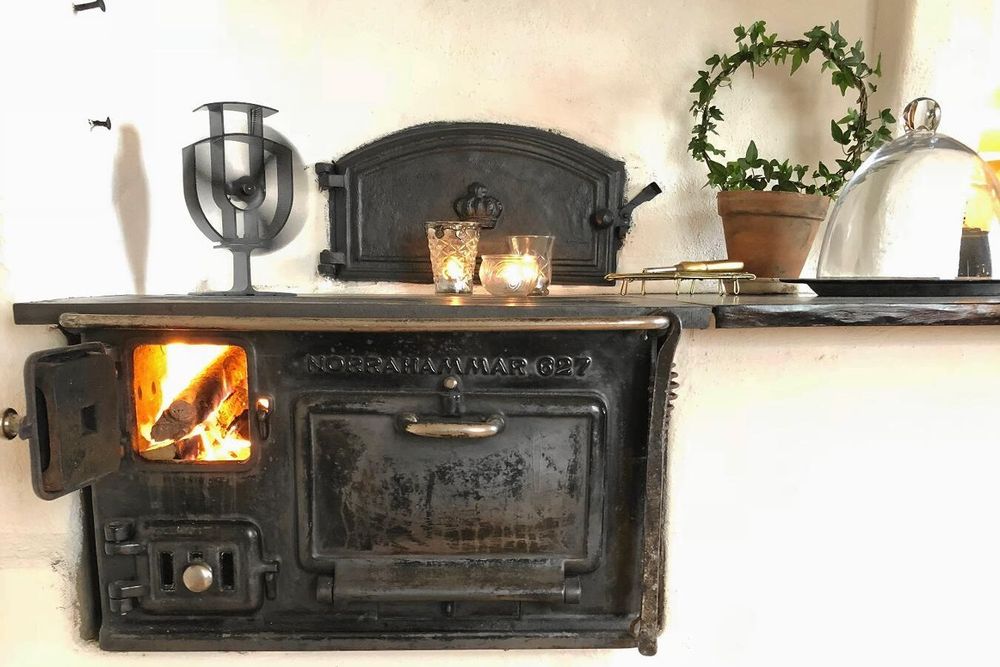 I köket värmer vedspisen med en kaminfläkt som sprider värmen.