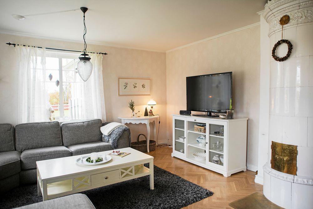 Vilsamma färger i vitt och grått i vardagsrumner med fin kakelugn.