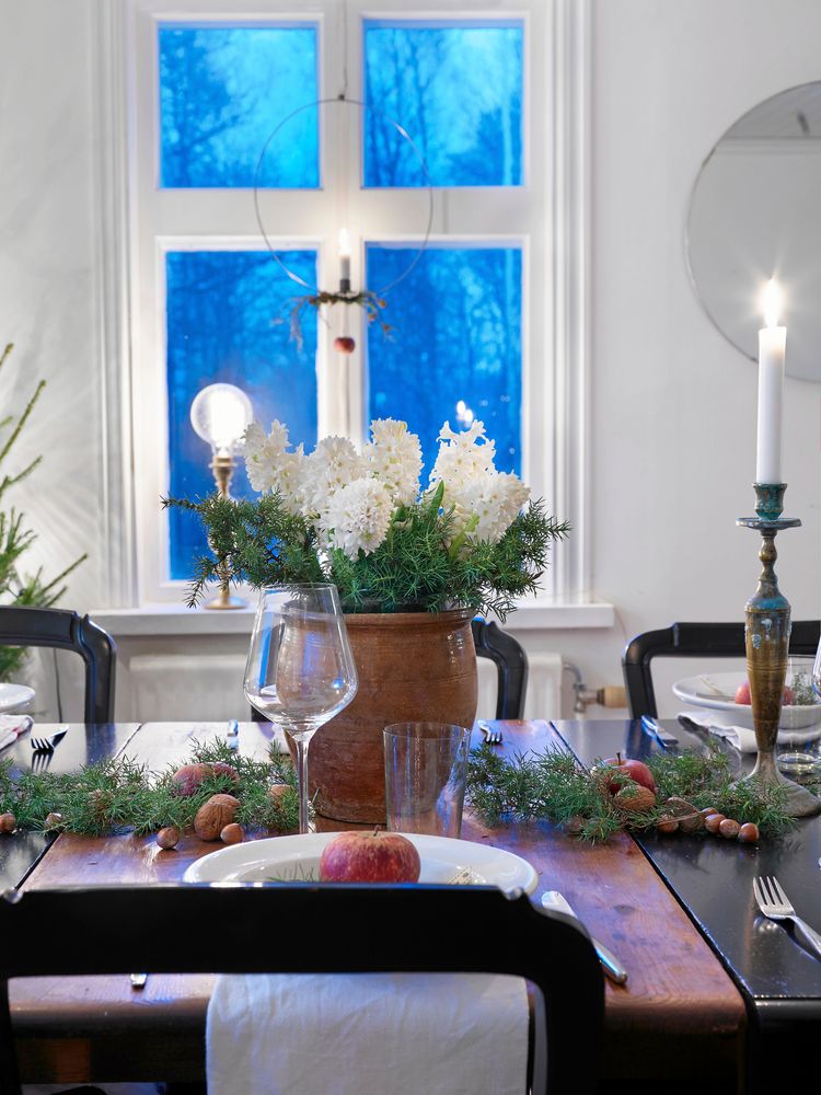 Anna har valt bort adventsstjärnor och elljusstakar i flera av fönstren och ersatt dem med ringar med levande ljus. På bordet står tulpaner, granris och äpplen.