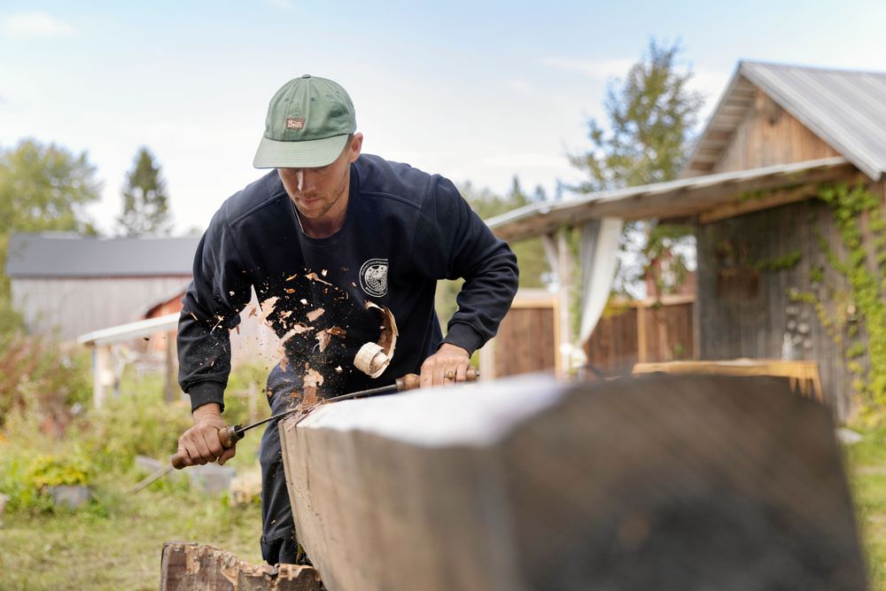 Med långa tag med bandknivens långa, böjda egg barkar Emil av den rejäla stocken.