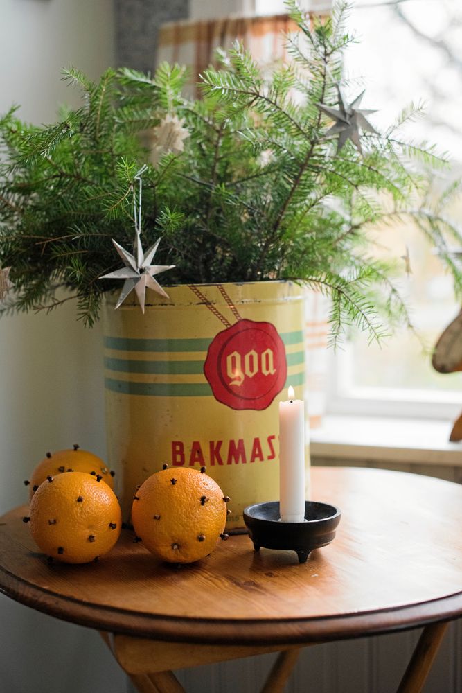 I en gammal retrobruk står friska grankvistar pyntade med minipappersstjärnor. Framför ligger apelsiner med kryddnejlikor.