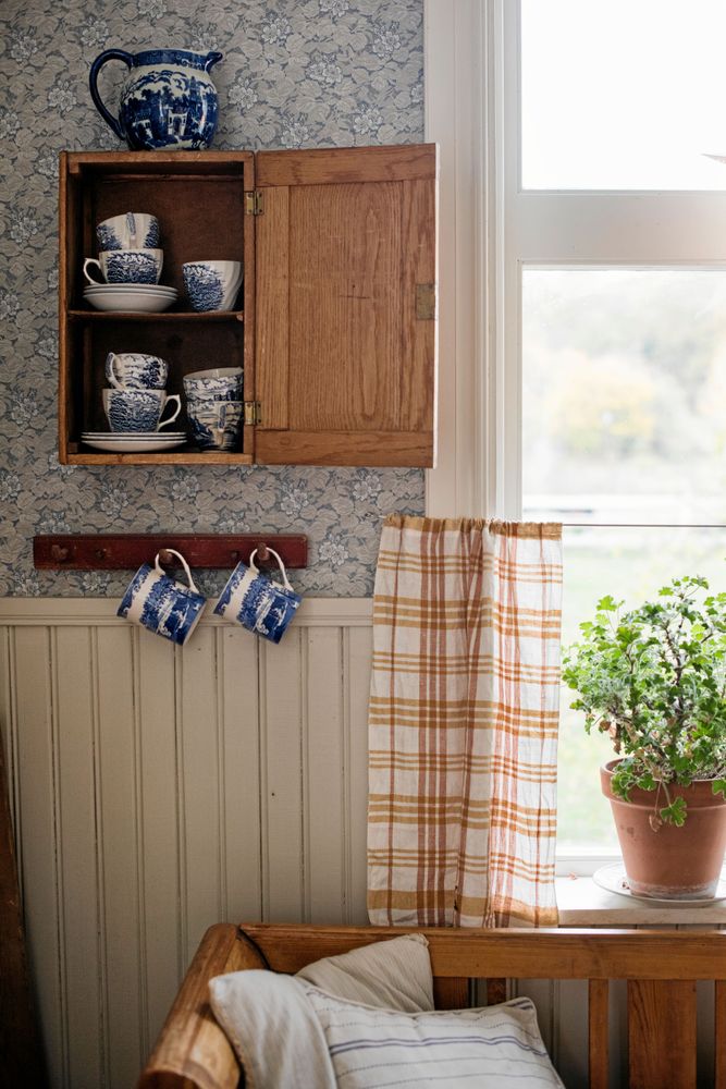 I det lilla skåpet samsas fina koppar som köpts på loppis. Den rutiga gardinen är också ett second hand-fynd.