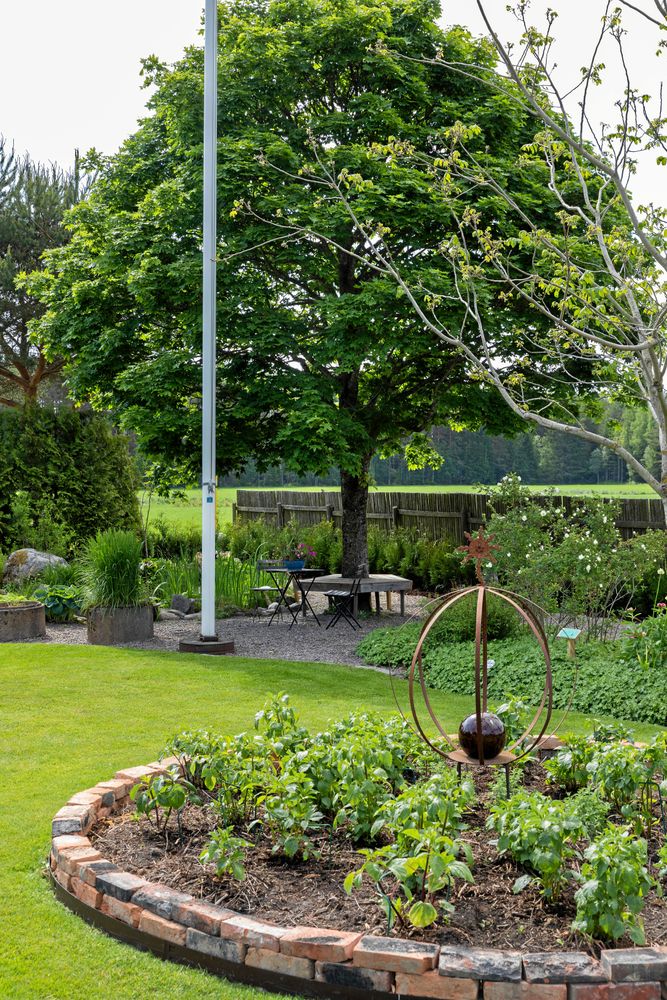 En vältrimmad gräsmatta håller ihop och lugnar ner i en trädgård med många olika växter, sittplatser och avdelningar.