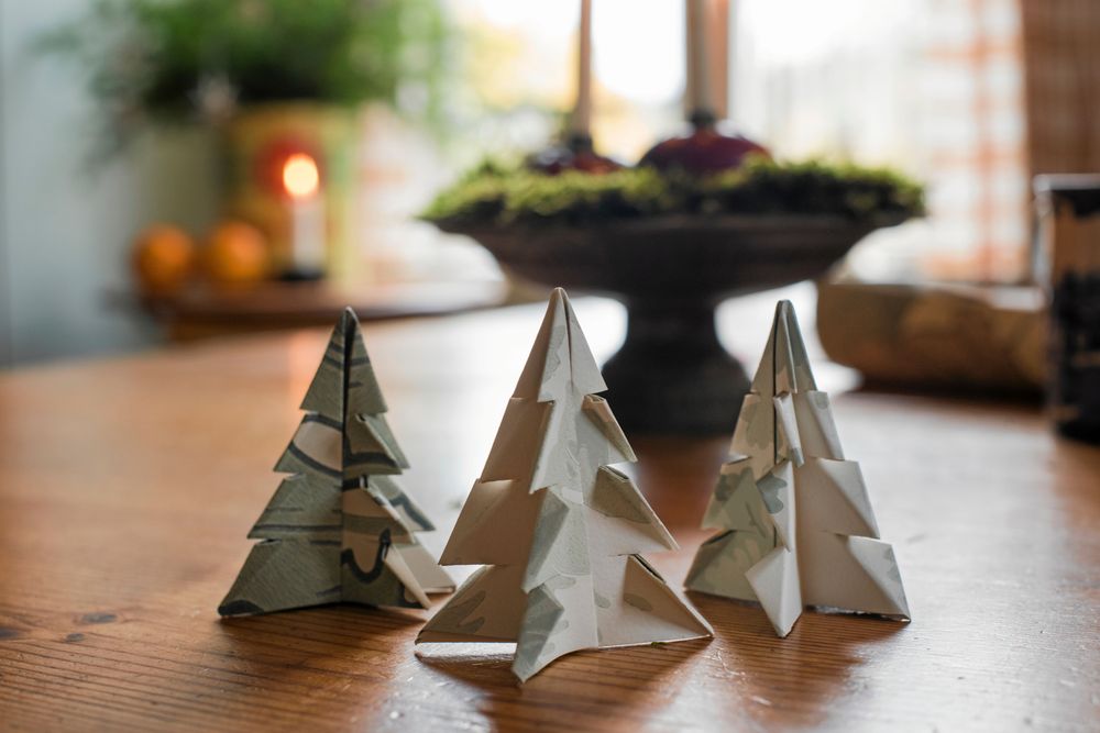 De små pappersgranarna som Johanna har vikt är fina juldekorationer. Bakom står adventsstaken med mossa och röda äpplen med levande ljus i.