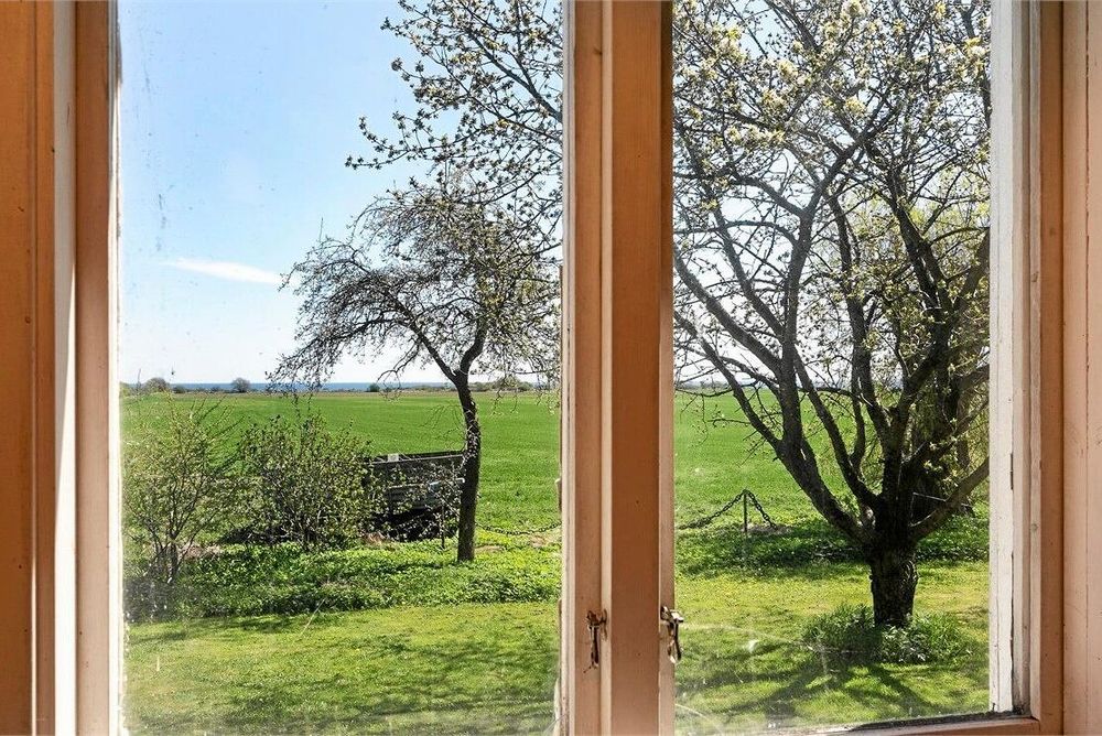 Genom fönstret blickar du ut över ängsmark och Östersjön.