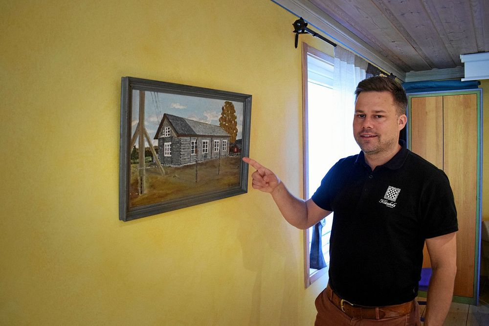 Andreas Johansson vid tavlan som visar upp den första byggnaden där det vävdes.