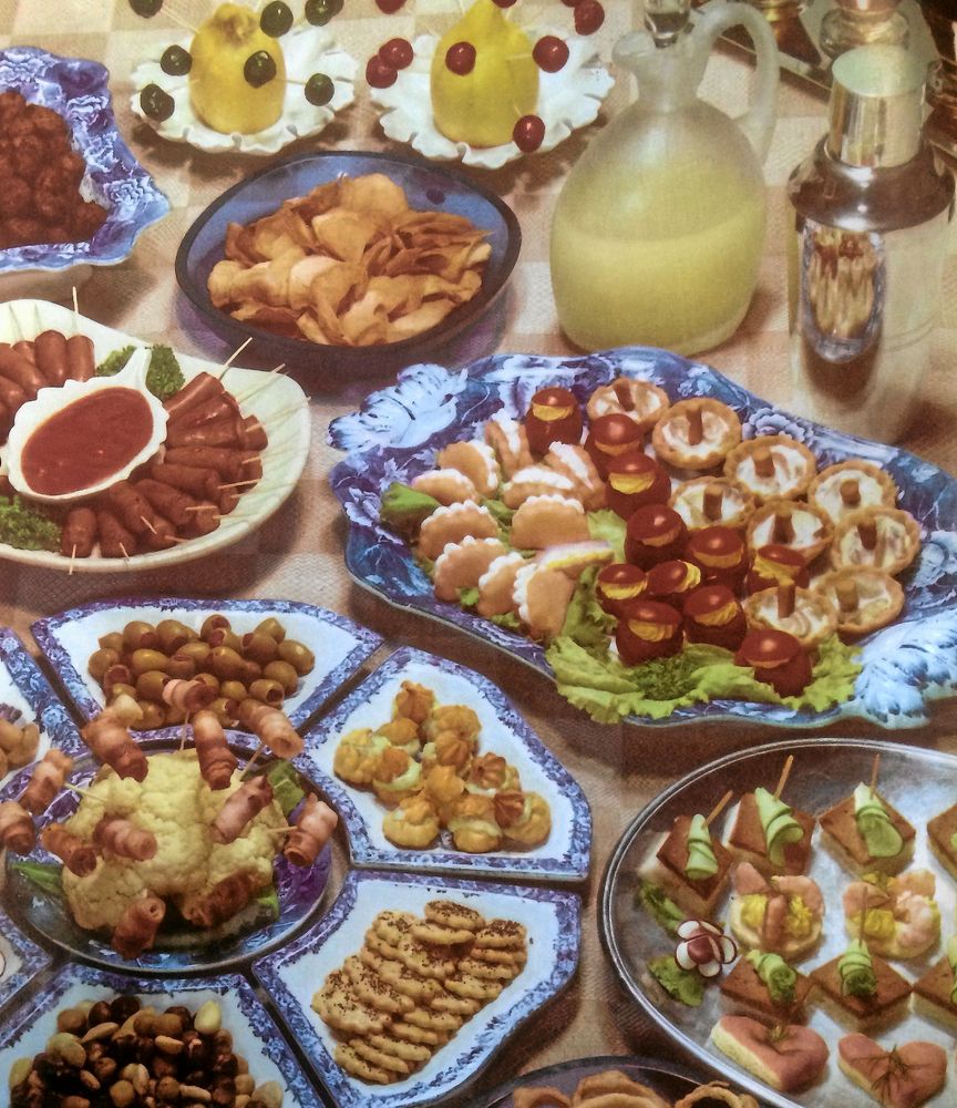 Att bjuda på cocktail med tillbehör var en skön konst. Här är det uppdukat med extremt välstajlad mat. Lägg särskilt märke till smördegssvamparna fyllda med styvning och den magnifika cabaretbrickan i blåvitt längst ner till vänster. Det är en ring av fat med diverse smågott runt ett blomkålshuvud med baconrullar på tandpetare.