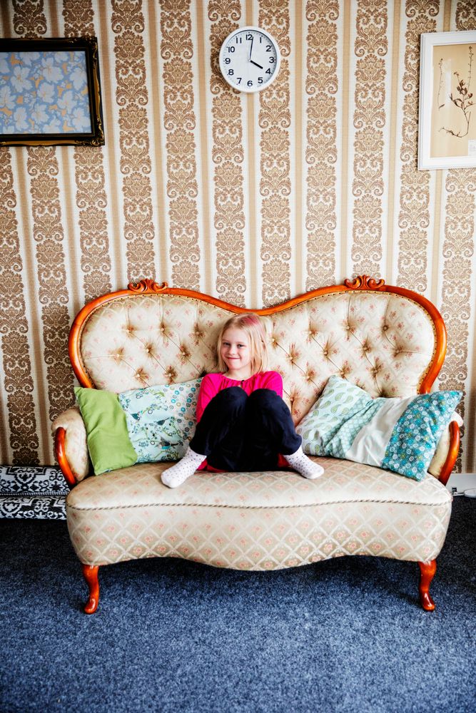 Felicia i gammelfarmors soffa som bevarats, med gammeldags tapet på väggen bakom.