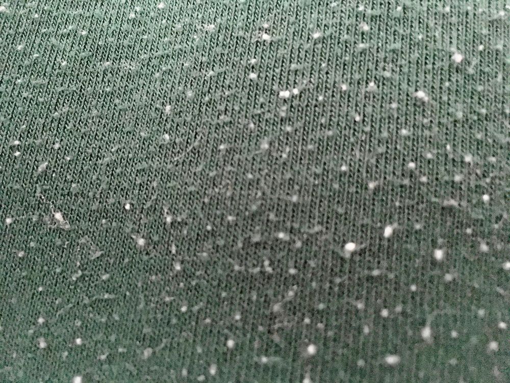 En noppig tröja har blivit luddad. Vita fibrer har fastnat i det gröna och gjort ont värre.