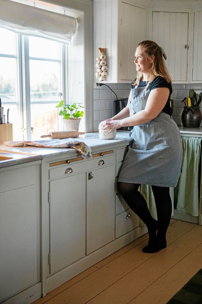 Kristin knådar degen i sitt stora kök med utsikt över åkrar och ängar.