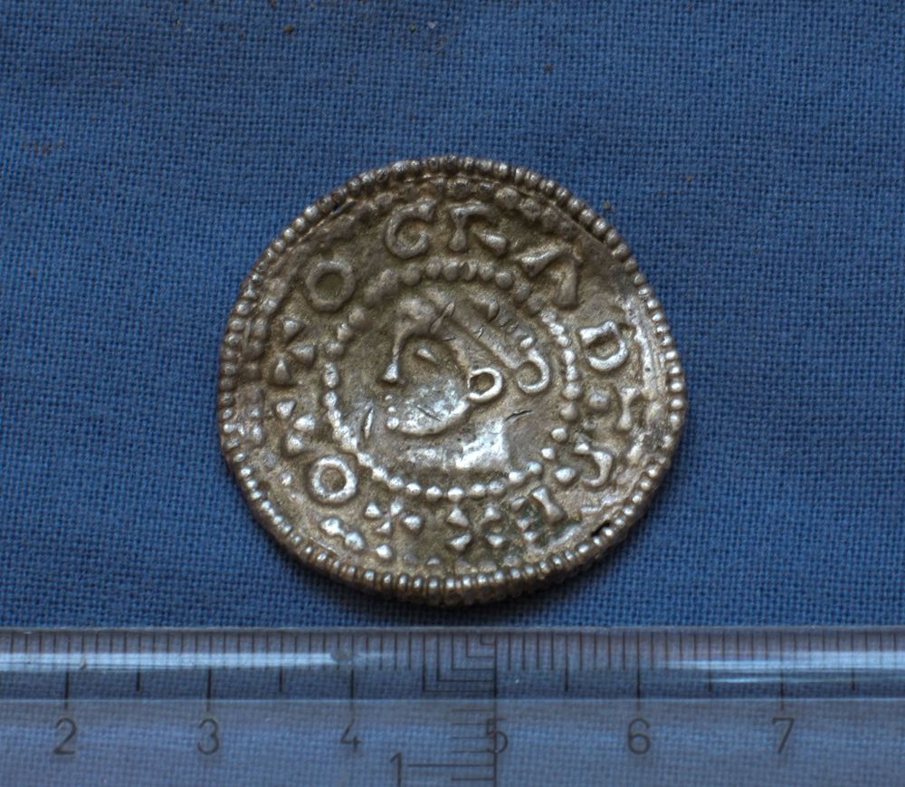 Ett av silversmyckena som hittades av markägaren, en så kallad brakteat, ett hängsmycke gjort av ett mynt. Namnet kommer från latinets uttryck för tunn plåt: bractea.